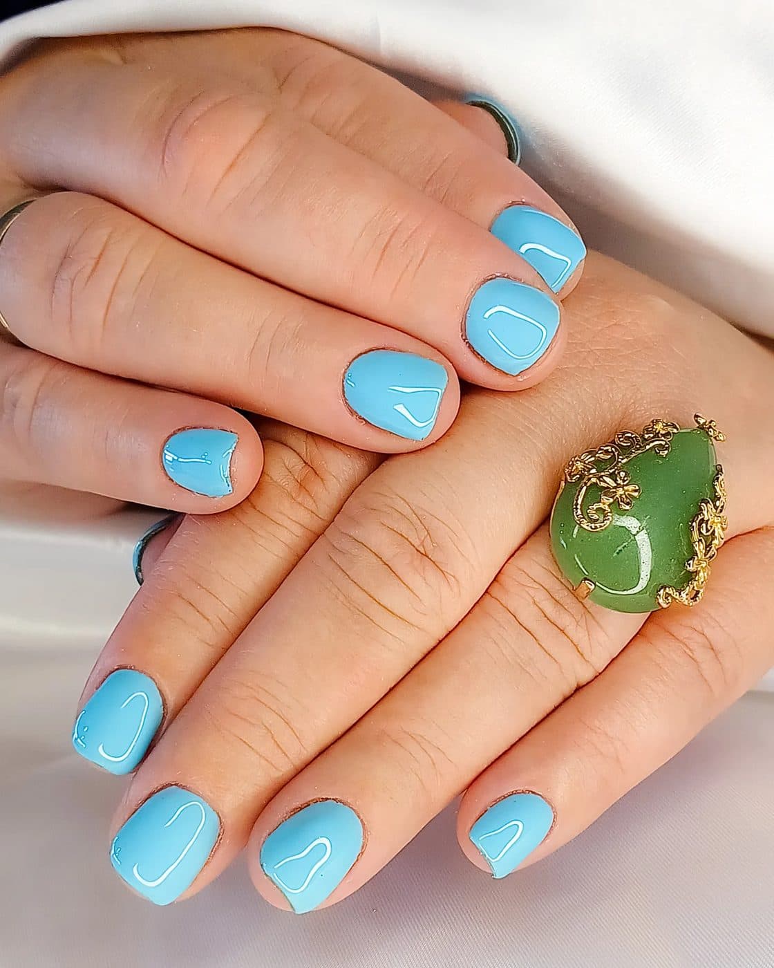 Unhas curtas em azul-claro e anel com pedra verde
